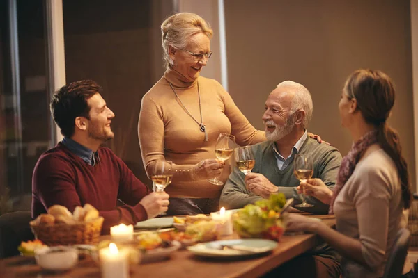 Happy family toasting with wine while having lunch at dining table. Focus is on mature woman.