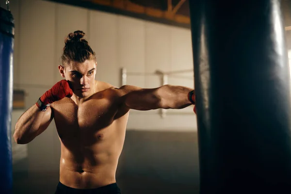 Young athlete hitting punching bag on boxing training in boxing club.