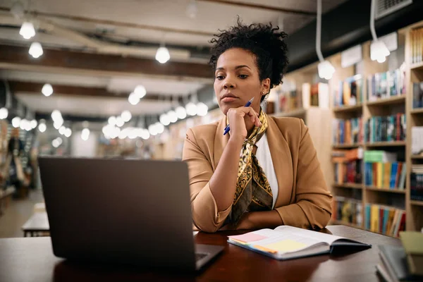 African American female professor using laptop while doing a research at university library.