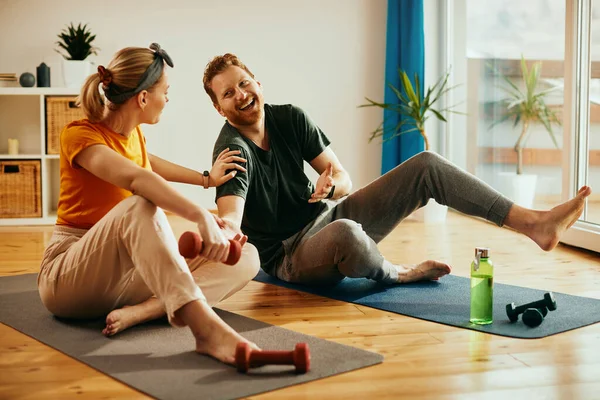 Cheerful man laughing and having fun with his wife while exercising with hand weights at home.