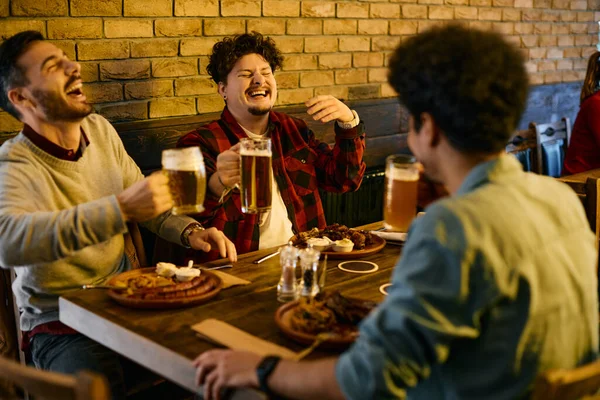 Young male friends having fun and laughing while drinking beer during their lunch in a pub.