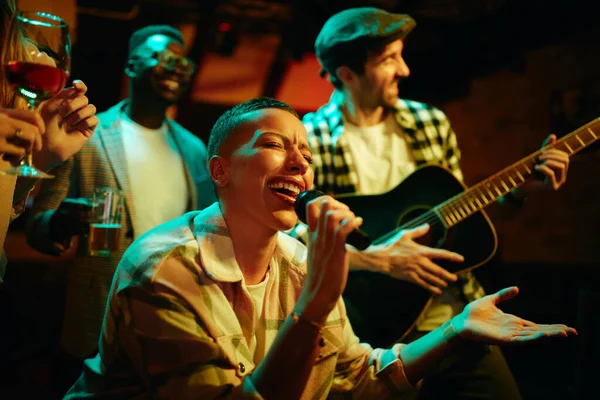 Young black woman singing on microphone during her night out in a pub.