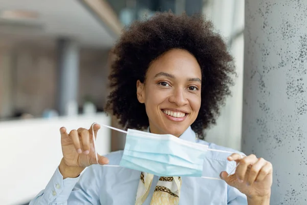 Happy African American female entrepreneur using protective face mask while standing in a hallway and looking at camera.