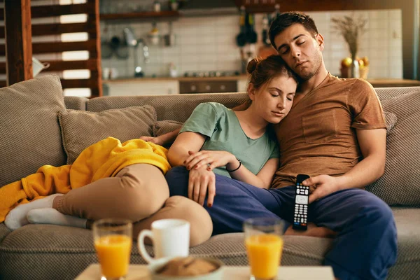 Tired couple fell asleep while watching TV in the living room.