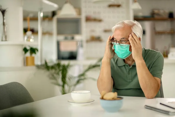 Pensive senior man with face mask feeling worried during social isolation due to coronavirus epidemic.