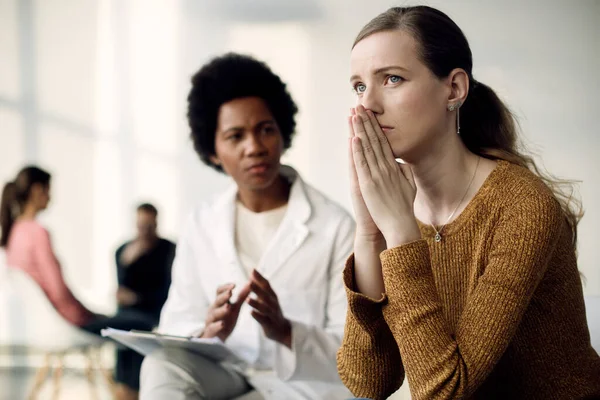 Sad woman thinking of something while mental health professional is talking to her during group therapy.