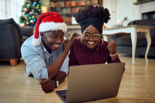 Young happy couple using laptop while having video call from home on Christmas. 