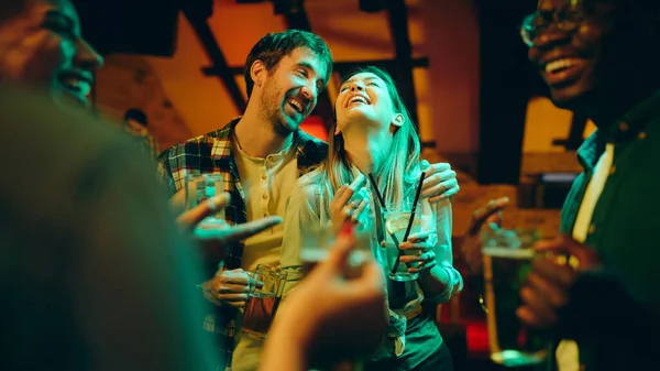 Young happy couple drinking and having fun with their friends in a bar at night.