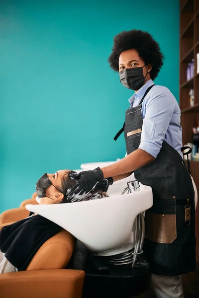 African American Hairstylist Washing Woman Hair Salon Looking Camera Wearing — Zdjęcie stockowe