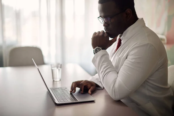 Pensive Black Doctor Using Laptop While Working His Office Clinic — Stok fotoğraf