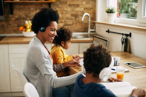Happy African American working mother homeschooling her two kids.