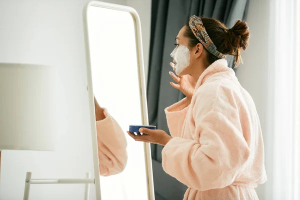 Young Woman Bathrobe Looking Herself Mirror Applying Facial Mask Home — Φωτογραφία Αρχείου