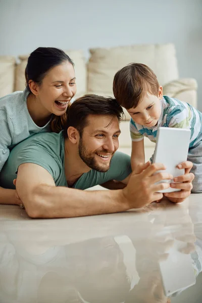 Cheerful family using digital tablet and taking selfie while having fun at home.