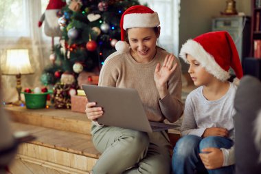 Happy woman using laptop with her son on Christmas and waving to someone during video call.