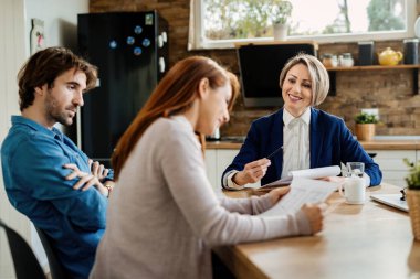 Mutlu emlakçı ve genç çift toplantı sırasında belgeleri inceliyor.. 