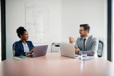 Happy businessman and his African American female colleague using laptops and communicating during a meeting the office. Copy space.