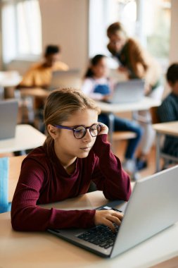 Elementary student e-learning on laptop while having computer class with her classmates at school.
