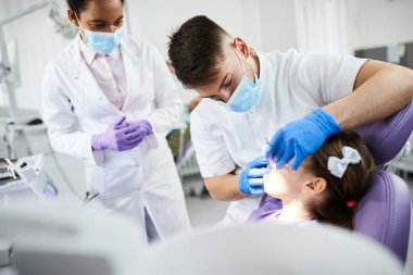 Little girl having dental examination at dentist's office. Focus is on dentist. 