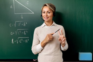 Female teacher standing in front of chalkboard and explaining mathematic during online class. 