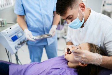 Little girl getting her teeth checked by male dentist during dental appointment.
