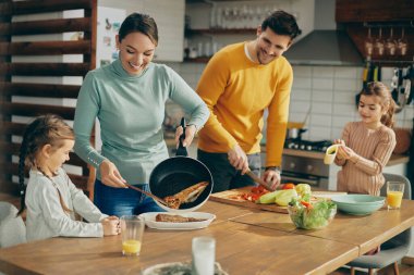Happy family having fun while cooking together and preparing healthy food in the kitchen. Focus is on woman. 