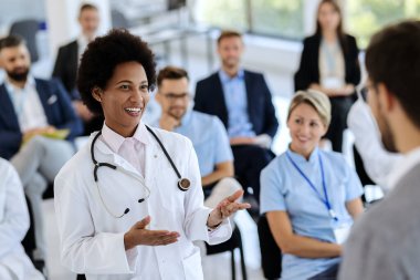 Happy African American female doctor talking to a businessman who is holding a seminar in convention hall. 