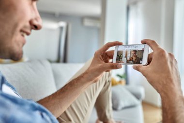 Close-up of a man using mobile phone while choosing online study program from home. 
