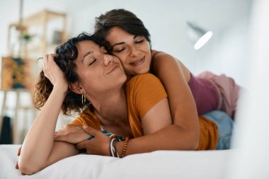 Young lesbian couple in love embracing with their eyes closed while relaxing on a bed. 
