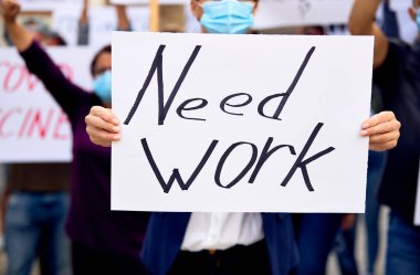 Close-up of female protester holding a placard with need work inscription after losing her job due to coronavirus pandemic. 