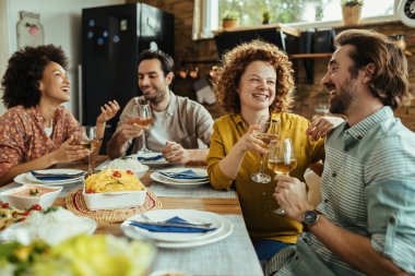 Group of happy friends having fun while drinking wine and communicating during lunch at home. Focus is on redhead woman. 