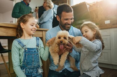 Two little girls and their father enjoying with a dog at home. 