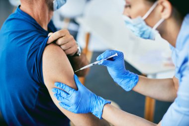 Close-up of nurse giving COVID-19 vaccine to mature man at vaccination center,