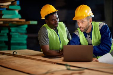 Manual workers cooperating while working on laptop at distribution warehouse.