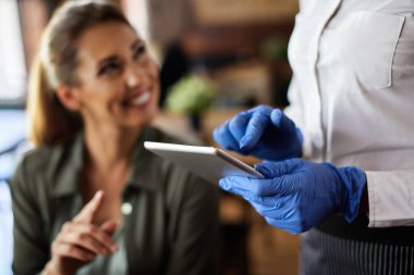 Close-up of waitress wearing protective gloves  while using digital tablet and taking order from customer in a cafe. 