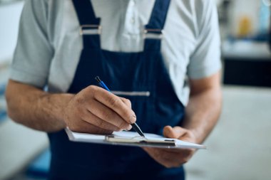 Close-up of auto mechanic taking notes while working in a workshop.