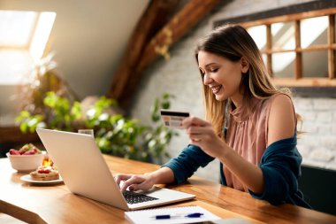 Happy businesswoman using credit card and checking her online bank account over laptop at home. 
