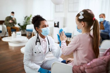 African American female dentist giving high-five to a little girl at dental clinic during COVID-19 pandemic.