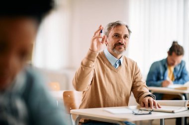 Mature student raising his hand to ask a question during a class at lecture hall.