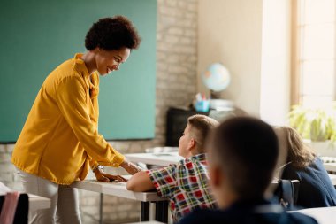 Happy black elementary teacher assisting her students with assignments during a class at the school. 