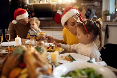 Noel günü yemek masasında aile yemeği yerken küçük kızını öpen bir anne.. 