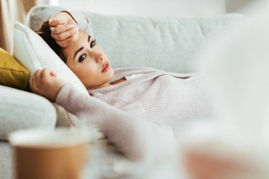 Young pensive woman feeling sad about something while relaxing on the sofa at home. 