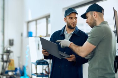 Otomobil tamircileri bilgisayar kullanırken konuşuyor ve araba atölyesinde çalışıyor.. 