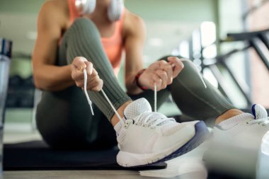 Close-up of athletic woman tying shoelace on her sneakers while preparing for workout at health club. 