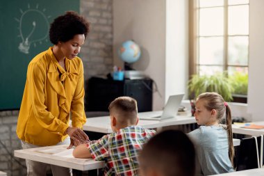 Black teacher assisting her elementary students during a class in the classroom. 