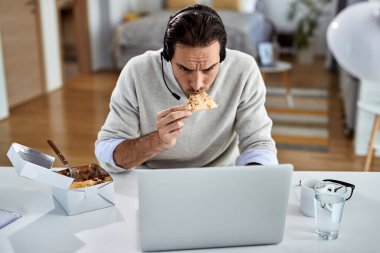 Young entrepreneur using laptop and eating while working at home. 