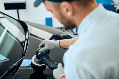 Close-up of mechanic polishing car hood while working in a workshop. 