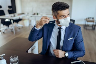 Young businessman working in the office and putting on a face mask due to coronavirus epidemic. 