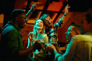 Young happy couple having fun while dancing and drinking with their friends in a bar at night. 