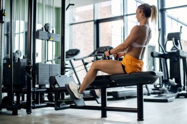 Low angle view of athletic woman having cross training on rowing machine at health club. 