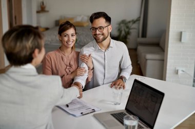 Young happy couple and real estate agent shaking hands on a meeting in the office. 